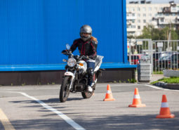 Woman L-driver driving slalom through the cones on training ground on small motorcycle