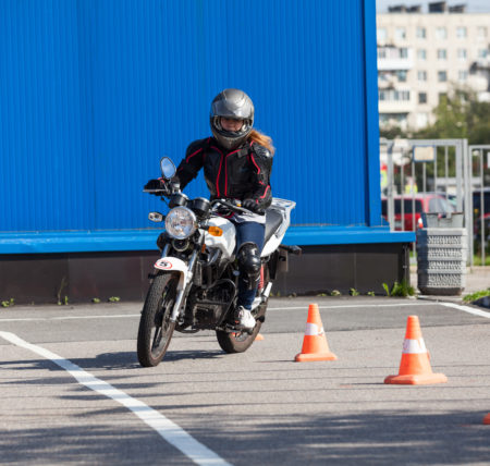Woman L-driver driving slalom through the cones on training ground on small motorcycle